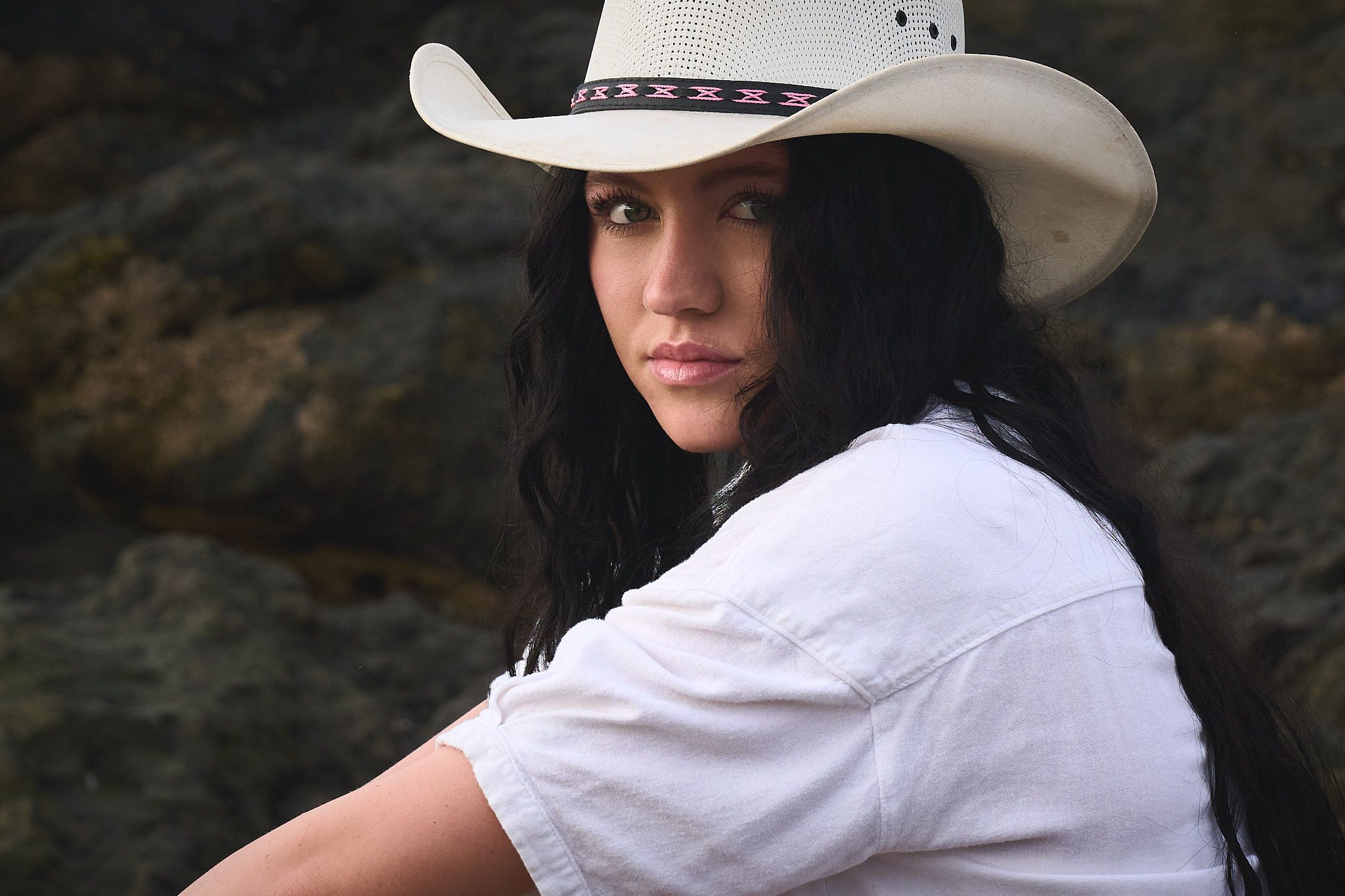 A person in a white cowboy hat and western attire poses against a dark background in a dramatic portrait.