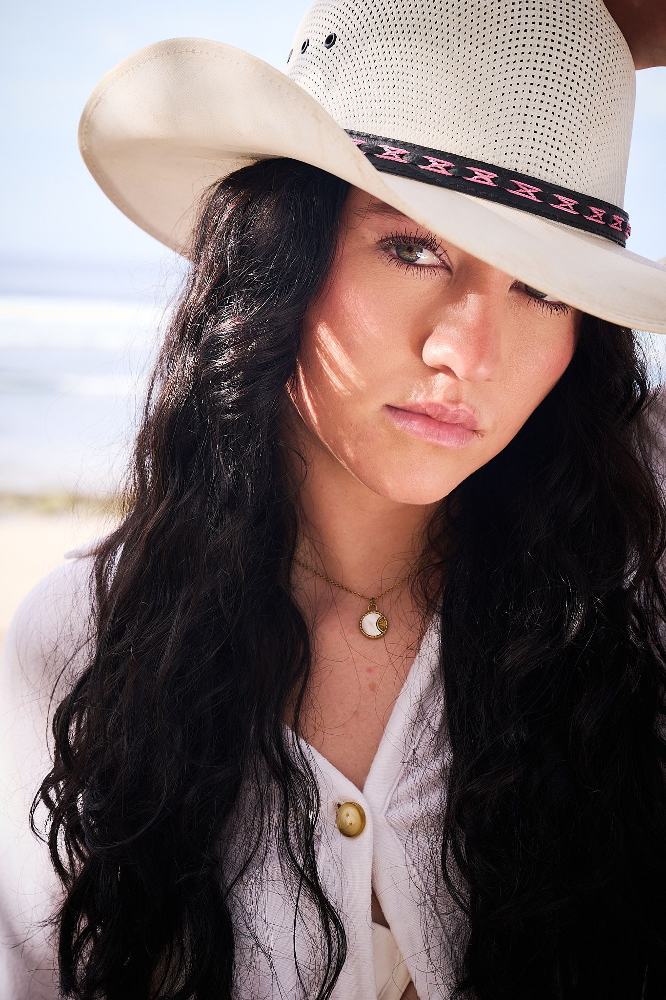 A person wearing a white cowboy hat with pink trim and dark flowing hair poses in a series of artistic selfies.