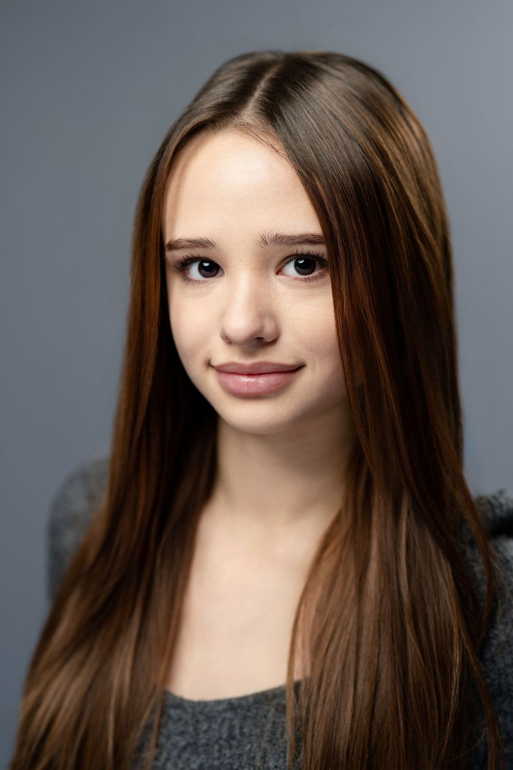 Young woman with long brown hair wearing a gray sweater poses for a portrait.