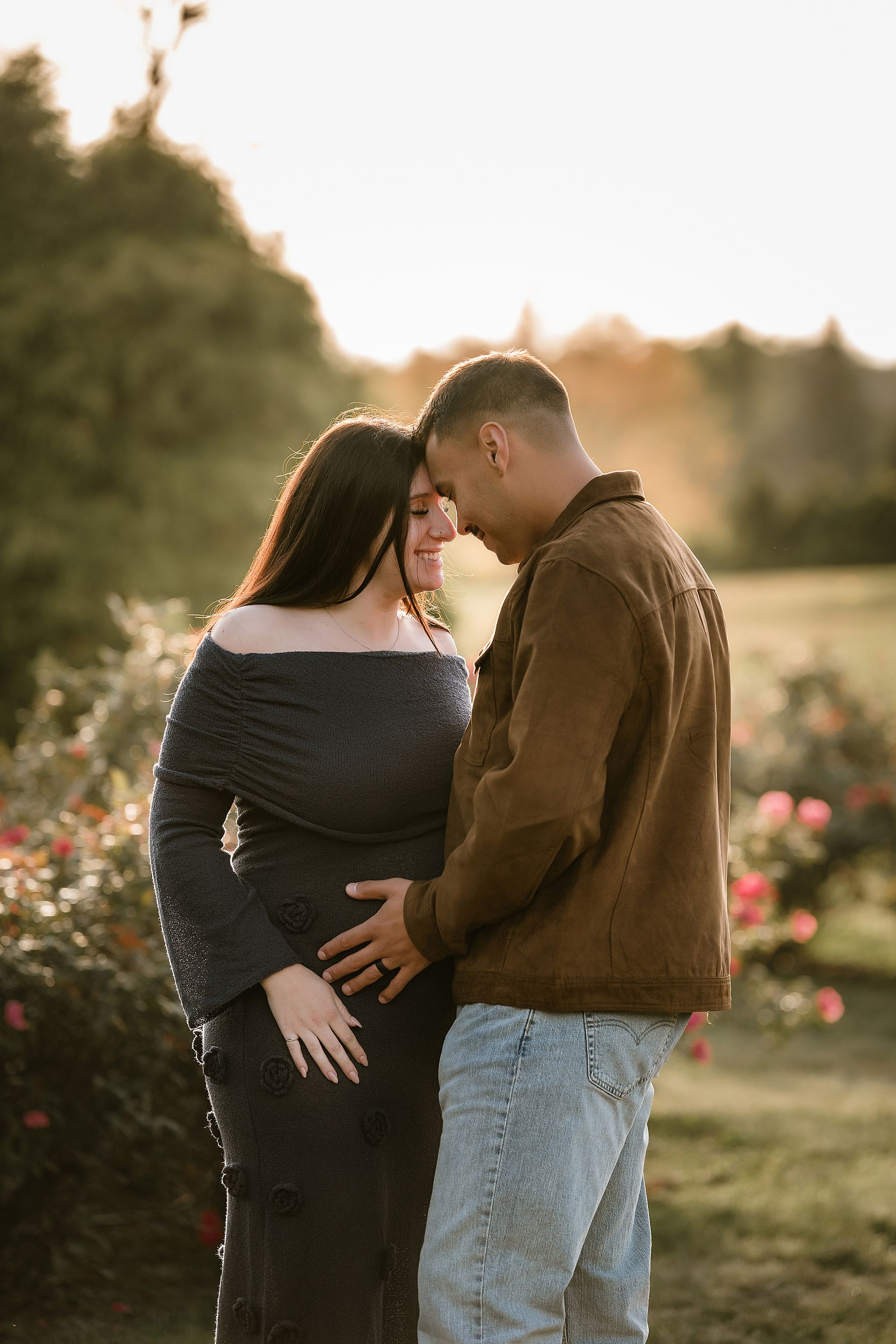 A couple shares an intimate moment in a garden at sunset with roses blooming nearby.
