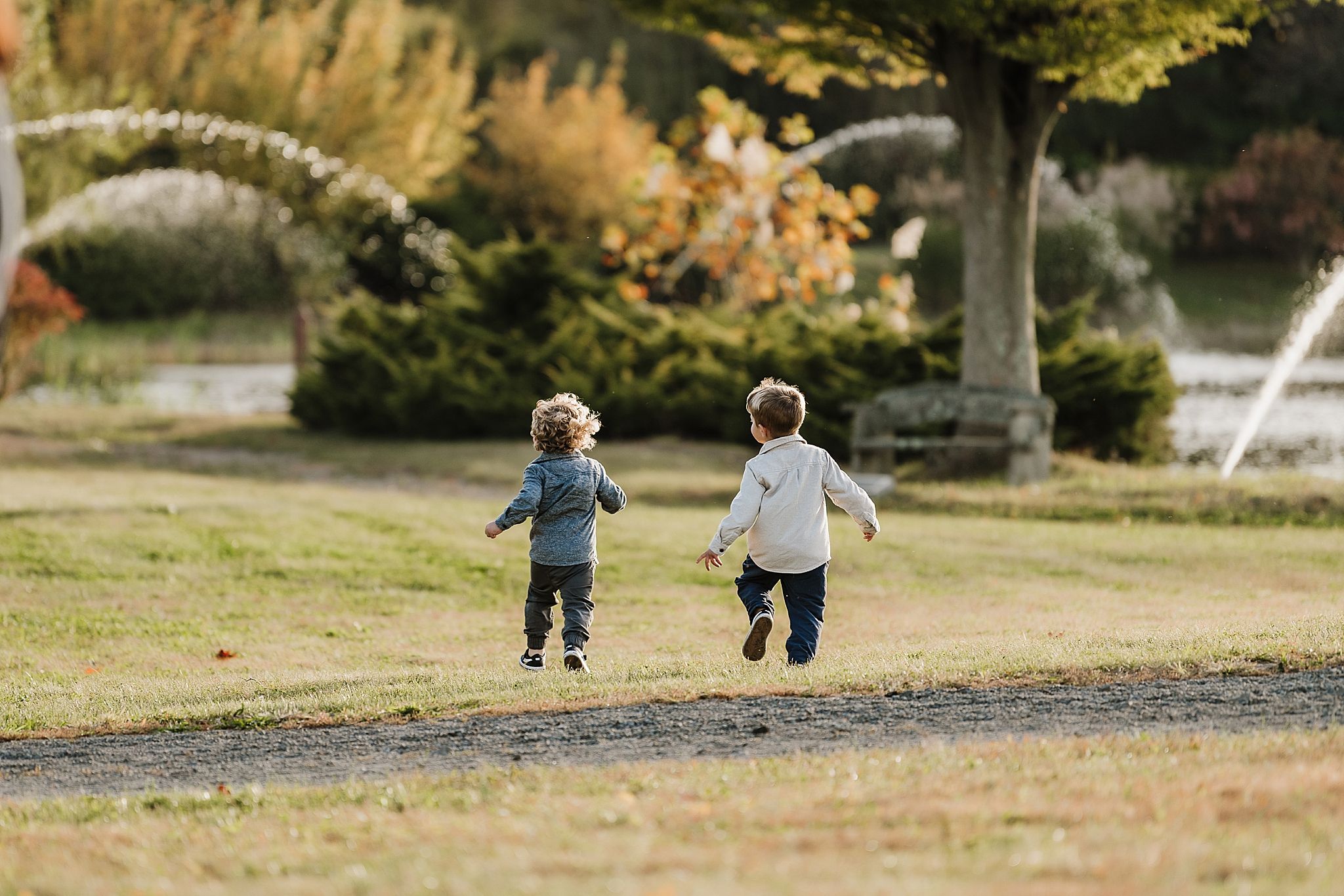 Two children run and play together on a grassy path during a sunny autumn day.