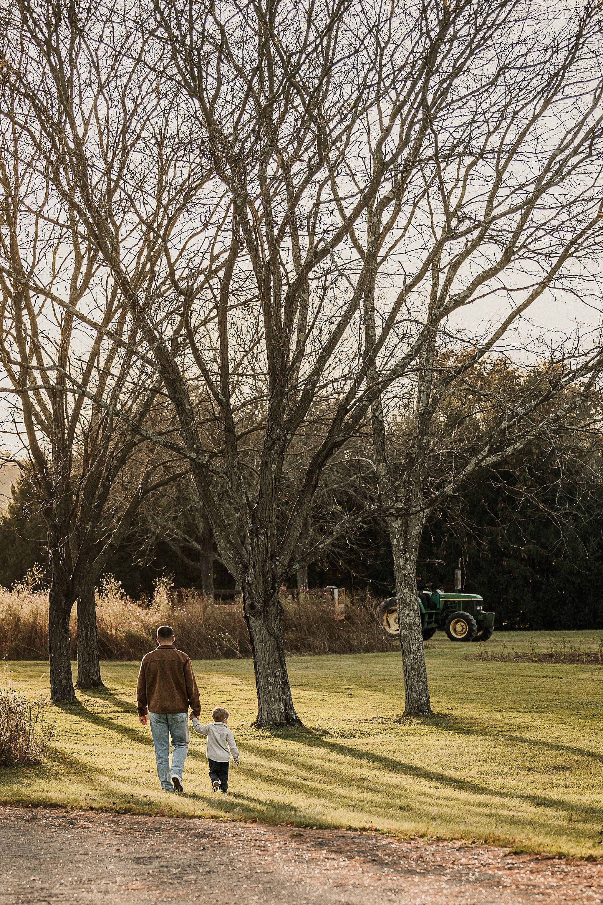 Two people walking together on a path through a scenic park with bare winter trees casting long shadows at sunset.