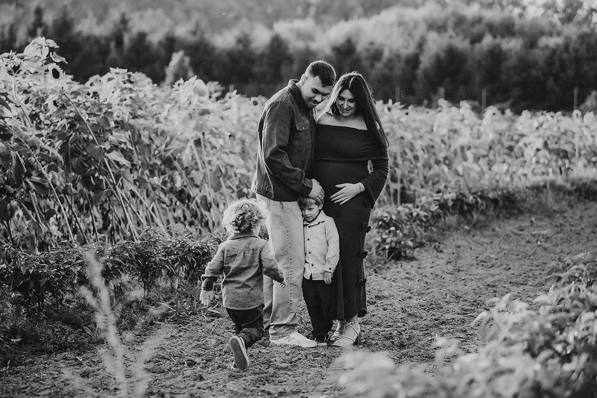 A family walks together through a scenic outdoor path surrounded by lush greenery and flowers in black and white.