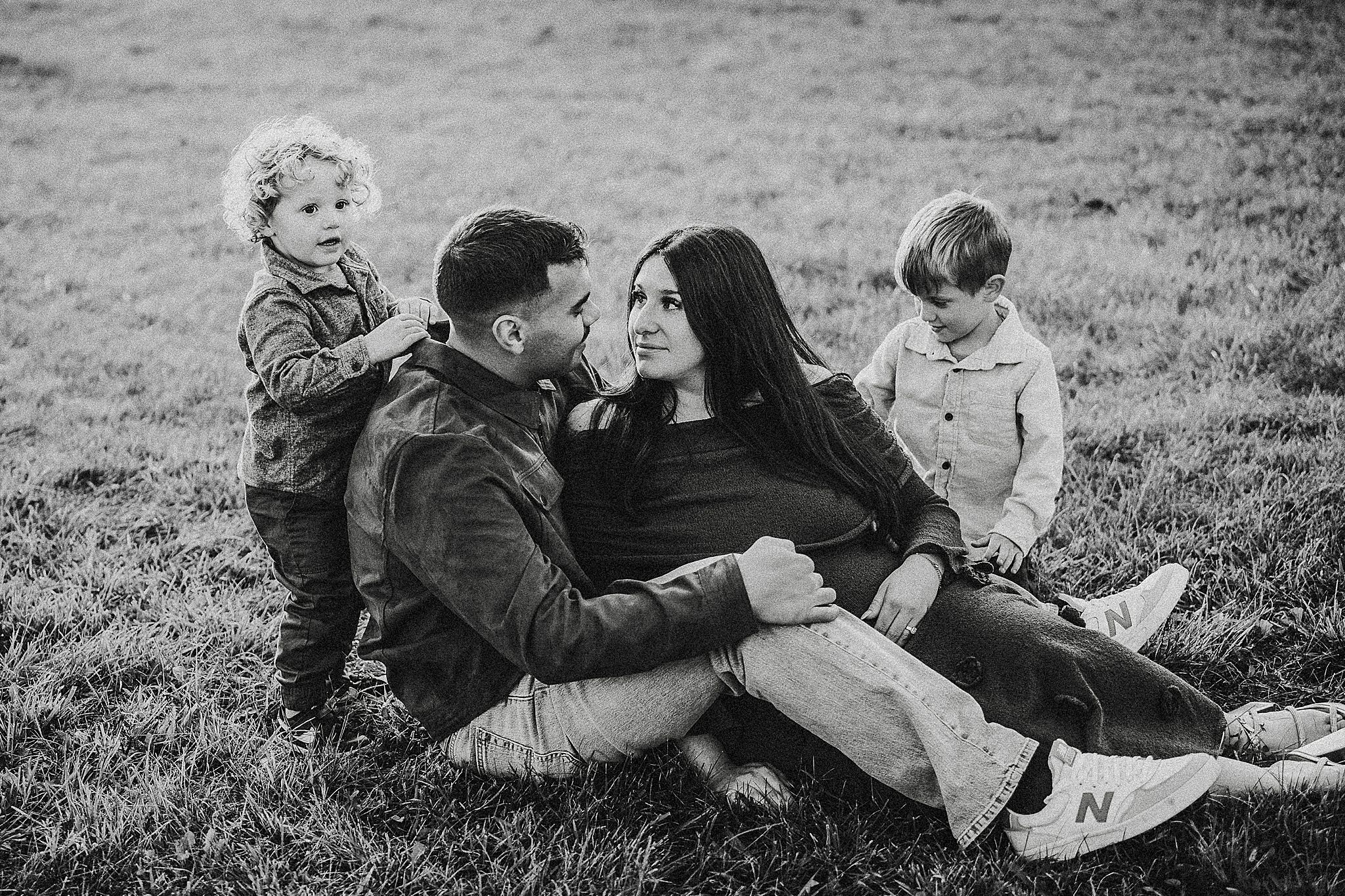 Black and white photo of a family relaxing together outdoors on grassy hill during a casual afternoon.