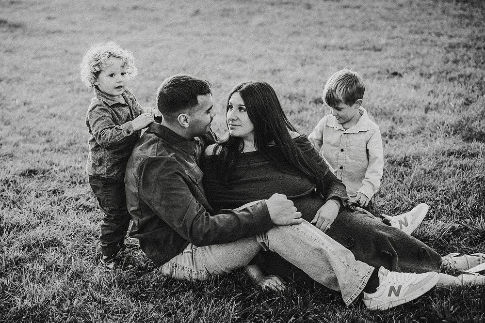 Black and white photo of a family relaxing together outdoors on grassy hill during a casual afternoon.