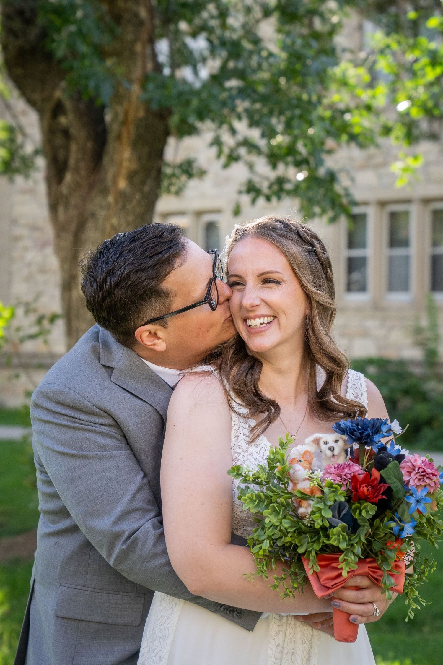 A joyful couple shares a tender moment outdoors with a vibrant wedding bouquet featuring blue and pink flowers.