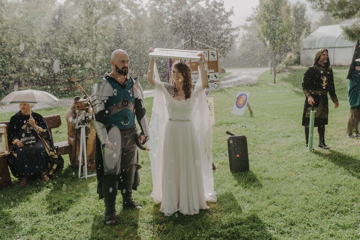 Bride and groom in medieval fantasy costumes walking together during a rainy outdoor wedding ceremony.