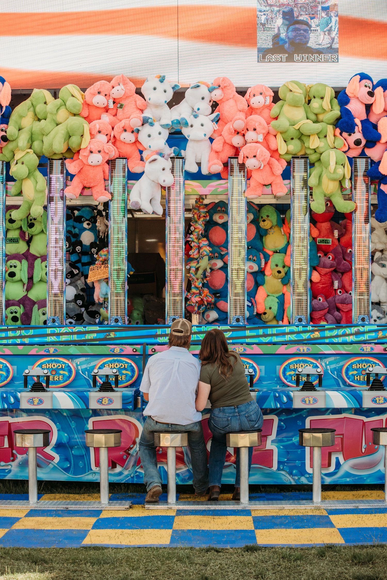 Colorful carnival game booth with hanging plush animal prizes and blue wave decorations at a fairground.