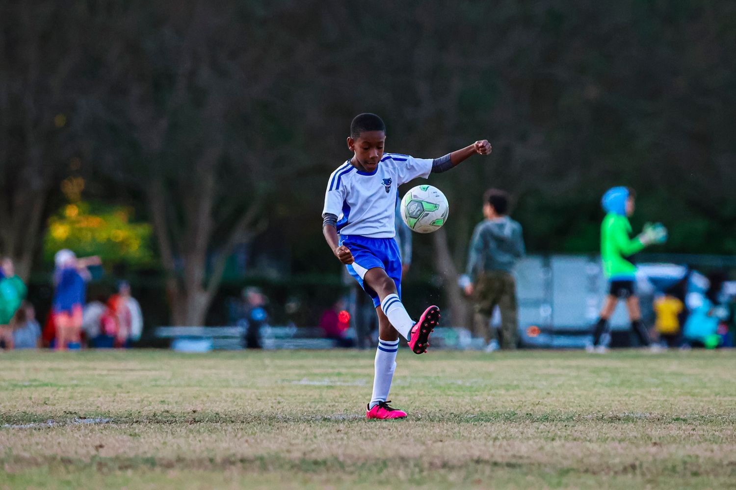 Soccer player in white jersey performs a jumping kick during an outdoor match on a grass field.