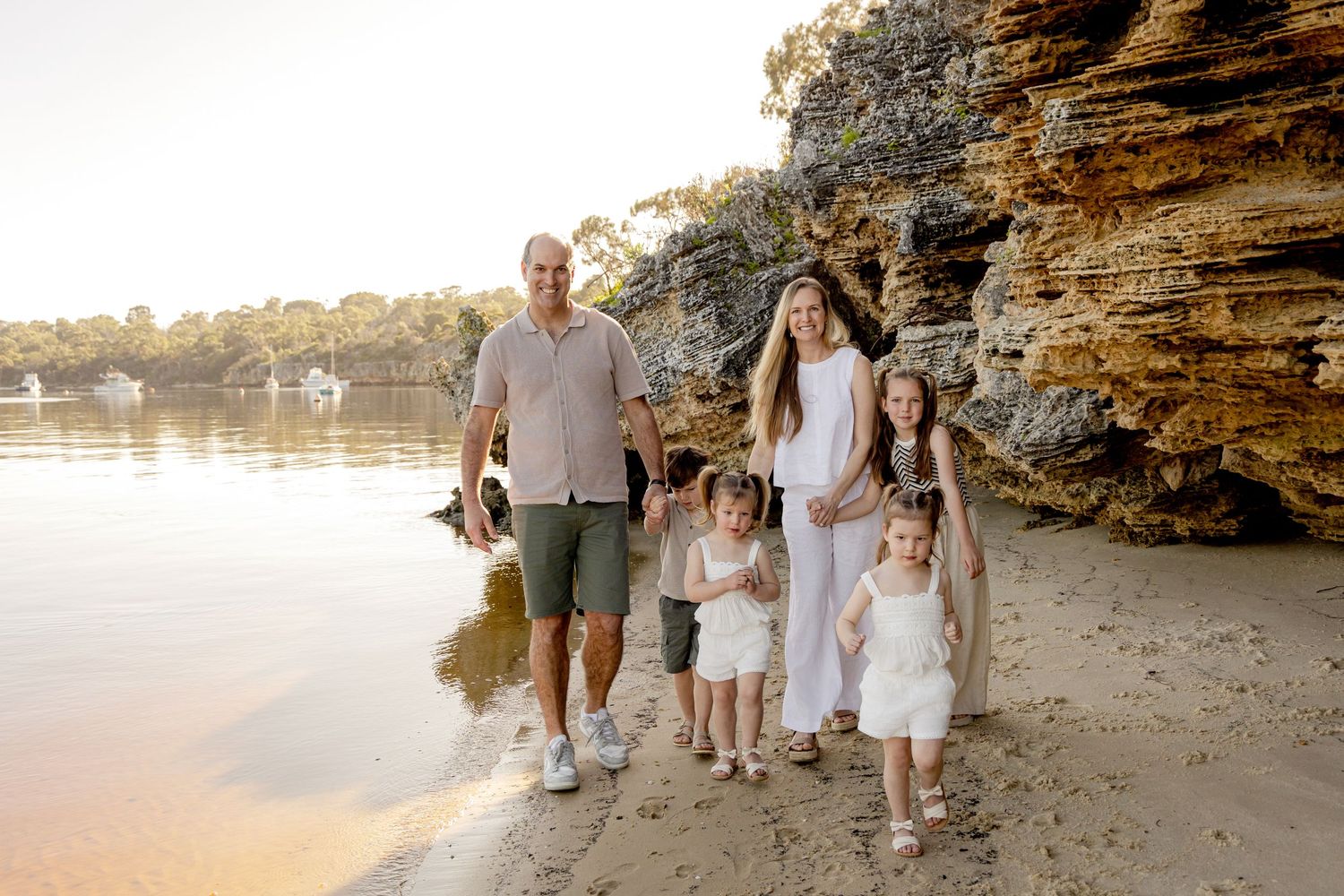 A family walks together along a rocky beach shoreline during golden hour sunset.