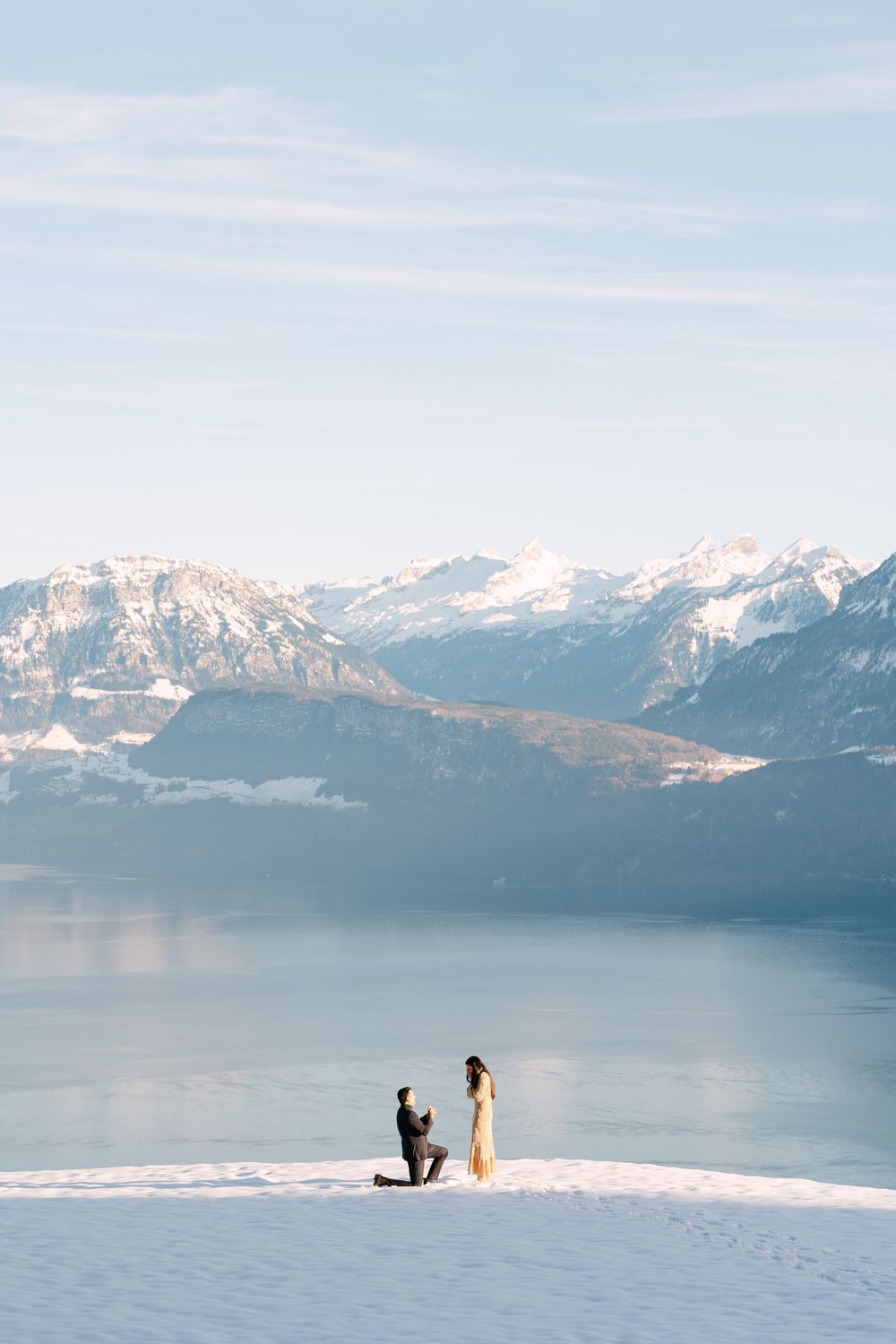 A scenic winter proposal moment against a backdrop of snow-capped mountains and a serene lake.