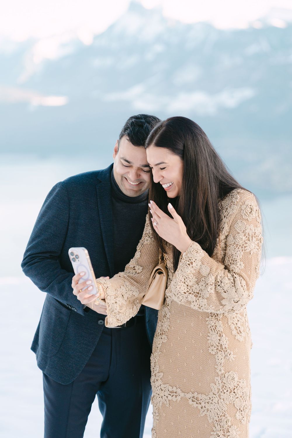 A couple shares a joyful moment together outdoors while looking at their phone.