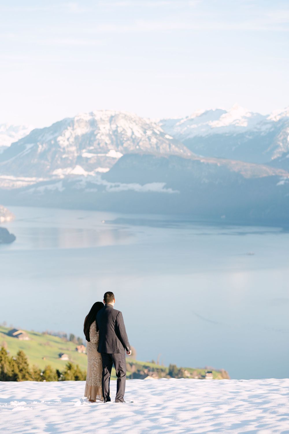 A couple walking together in the snow with a stunning mountain lake and snow-capped peaks in the background.