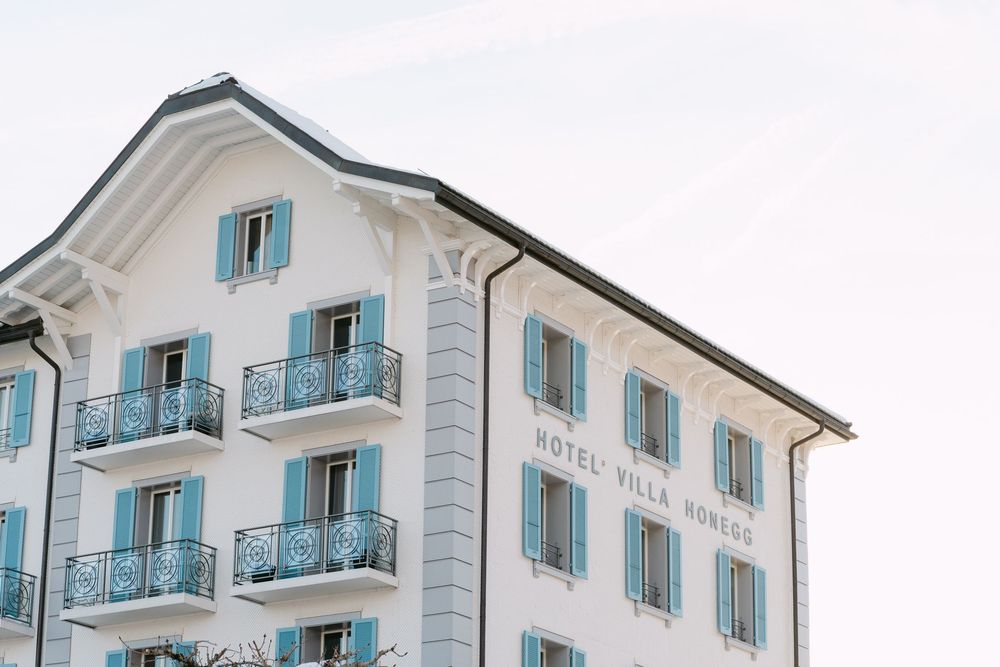 Elegant white hotel building with turquoise shutters and ornate balconies against a bright sky.