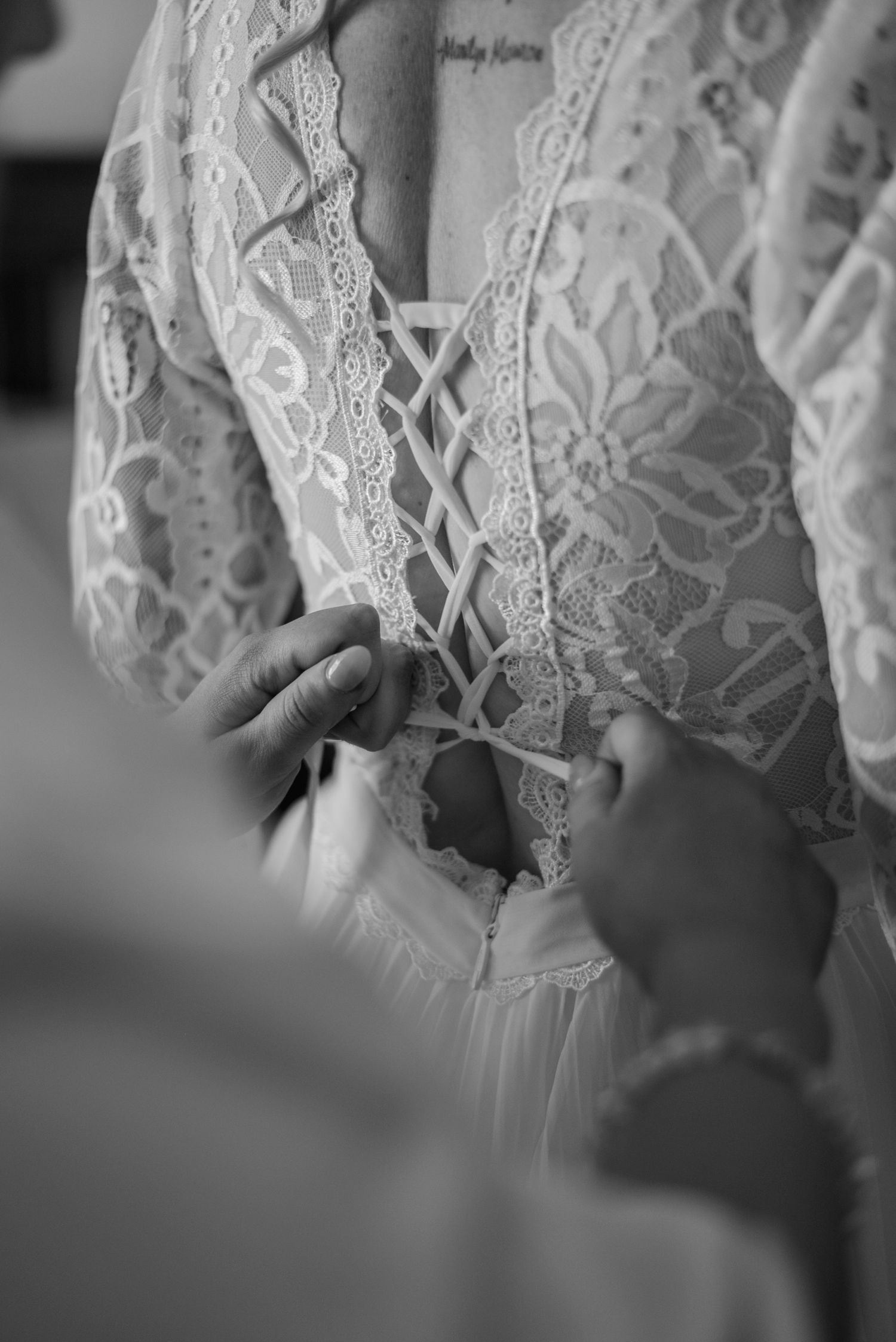 Close-up detail of delicate white lace and beading on a wedding dress bodice shown in black and white photography.