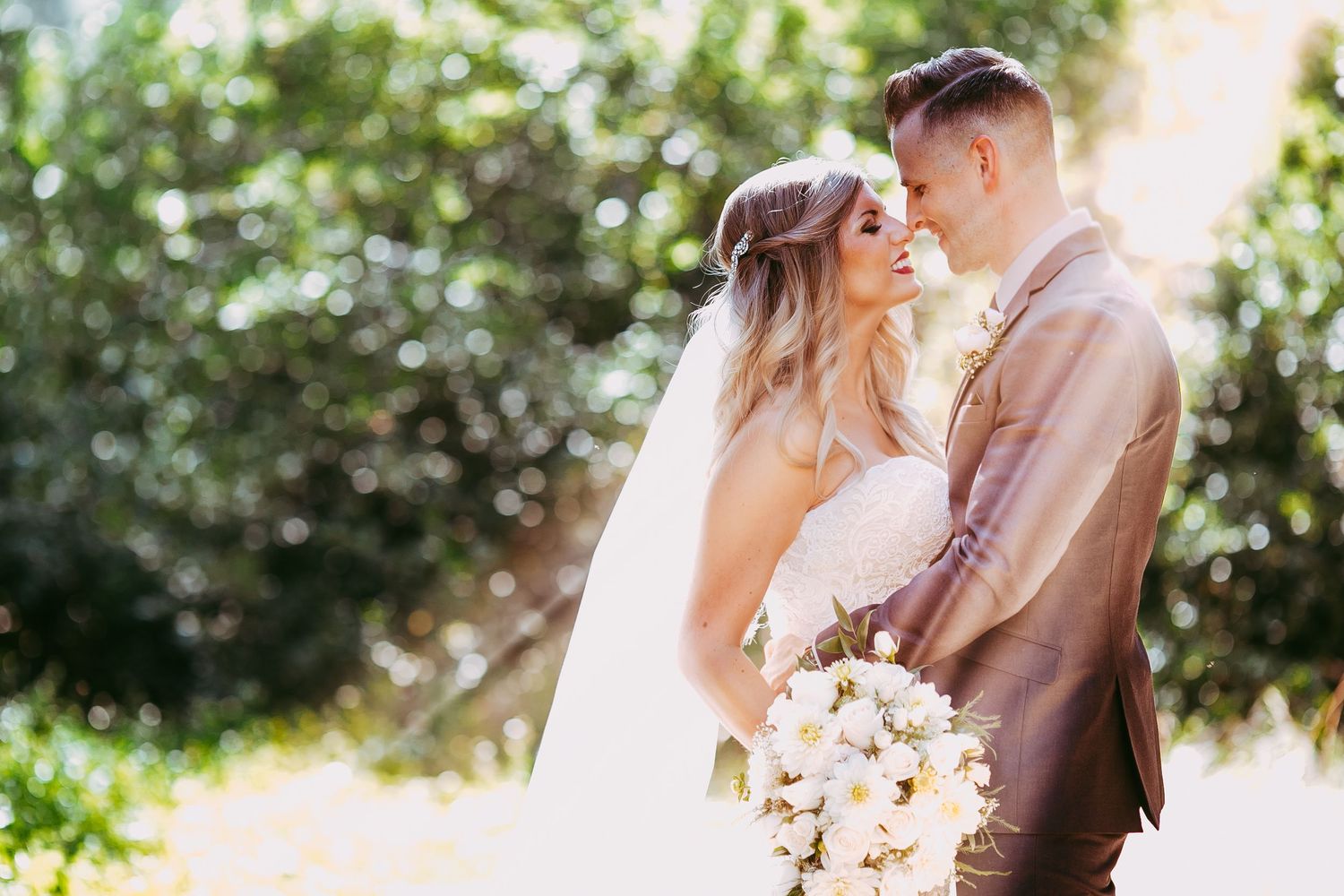 A couple shares an intimate moment during their outdoor wedding ceremony surrounded by greenery and sunlight.