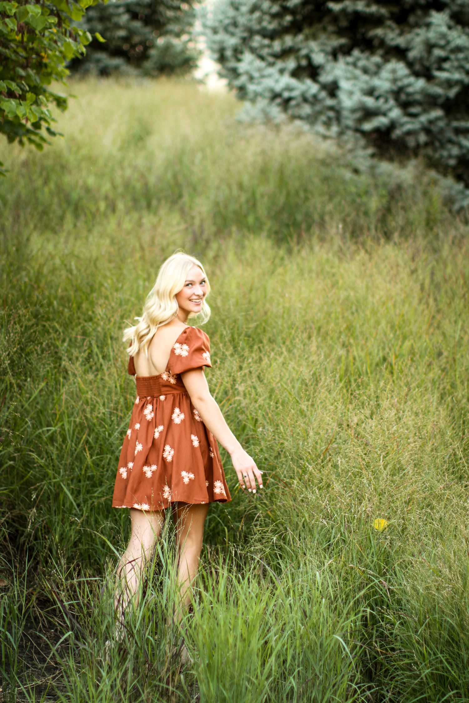A young woman looks over her shoulder as she frolics through a tall field of green grasses during her Kansas City senior photos.
