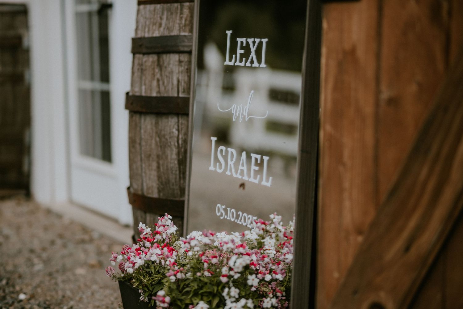 Rustic wooden barrels and pink flowers decorate the entrance of a winery or tasting room.