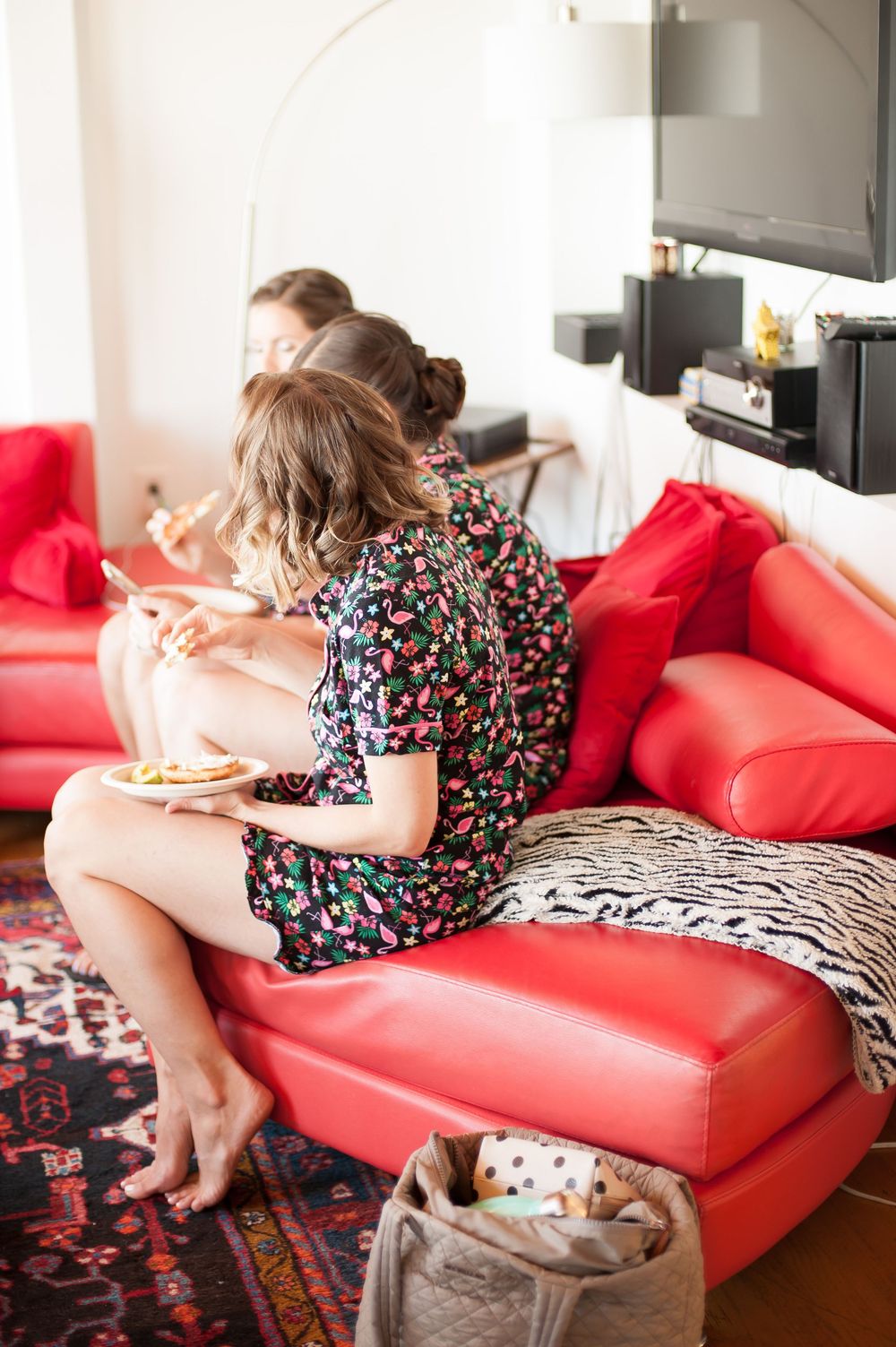 A person in a floral dress relaxes on a bright red leather couch with decorative pillows and a patterned rug below.