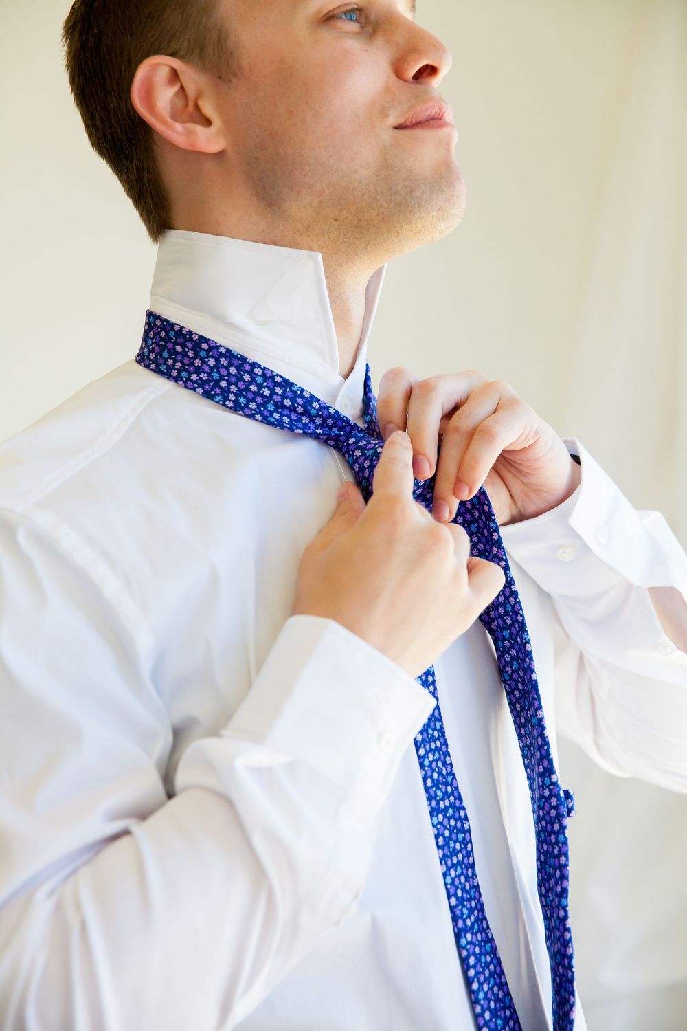 Someone adjusting a blue polka dot tie while wearing a crisp white dress shirt.