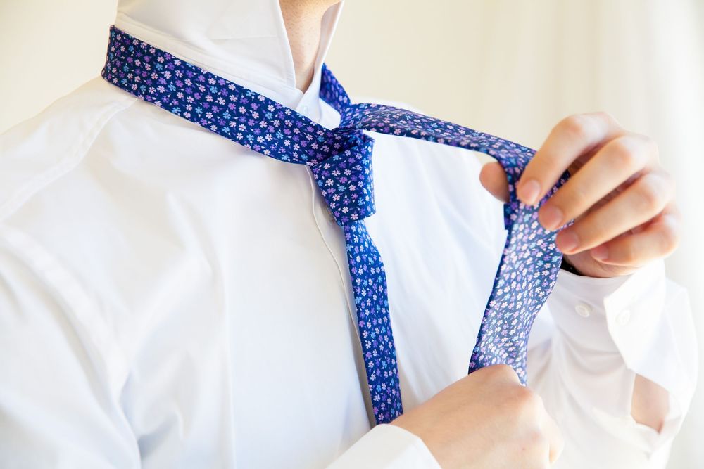 Close-up of hands tying a blue polka dot necktie against white shirt.