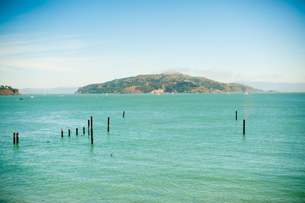 Turquoise waters of a bay with wooden pilings and hills in the background.