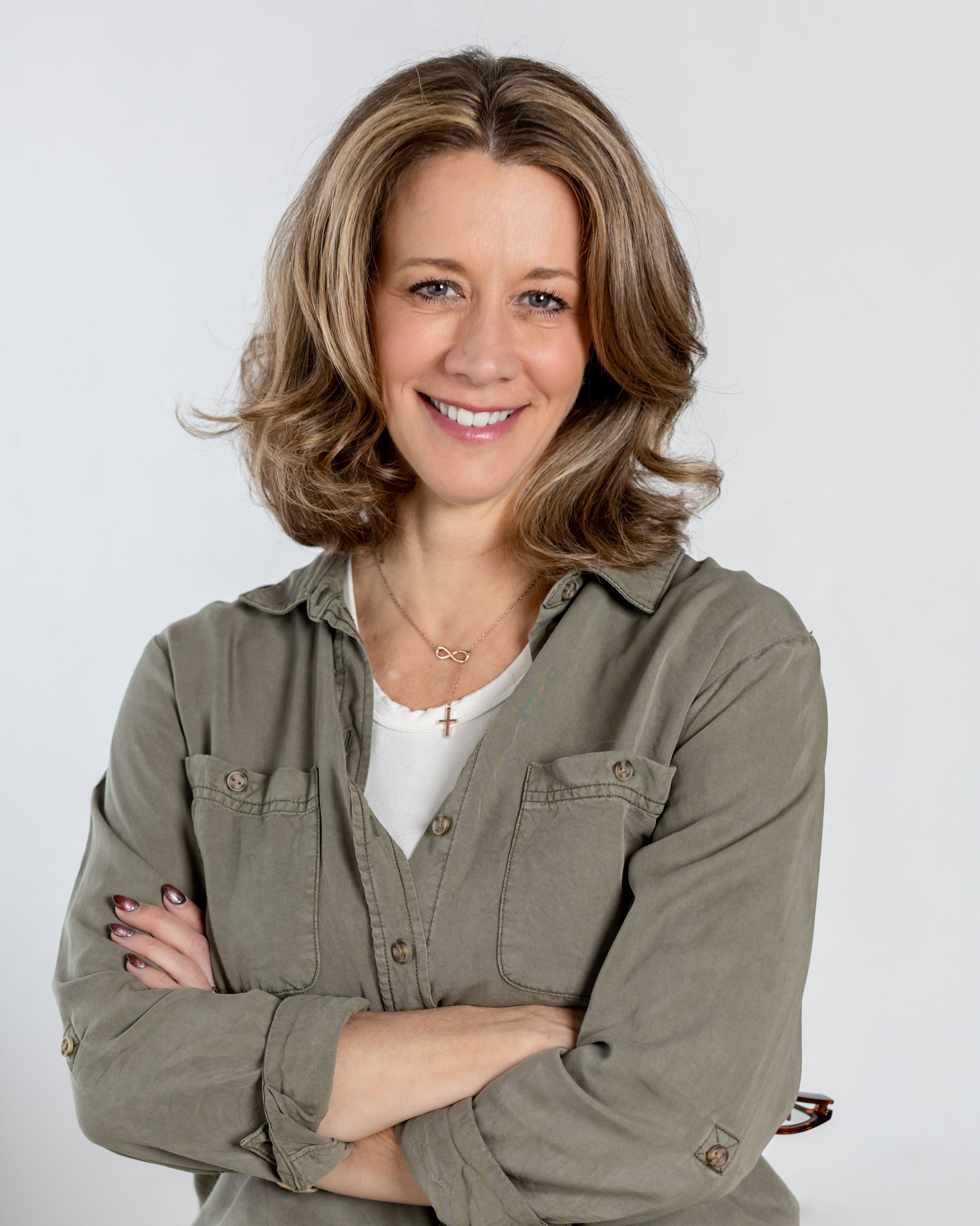 A person wearing a casual olive green button-up shirt poses confidently against a light background in a studio setting.