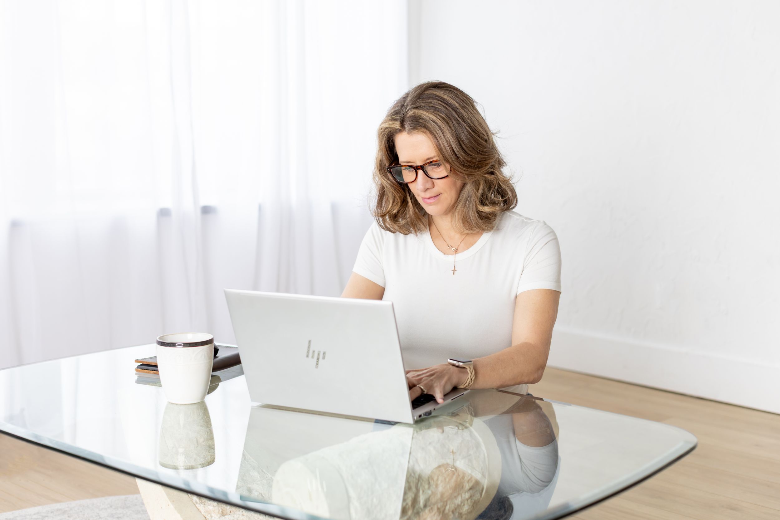 Person working on laptop at white desk while sitting on couch in bright modern room.