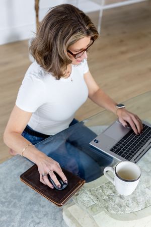 Person working on digital devices with laptop and tablet while having coffee on a marble table surface.