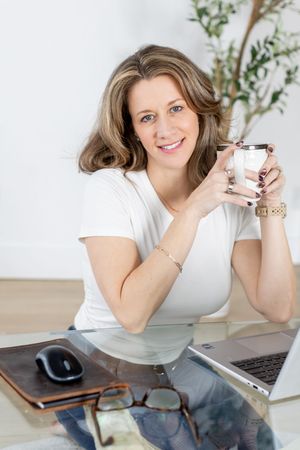 Professional working at desk with laptop and coffee cup in bright modern workspace setting.