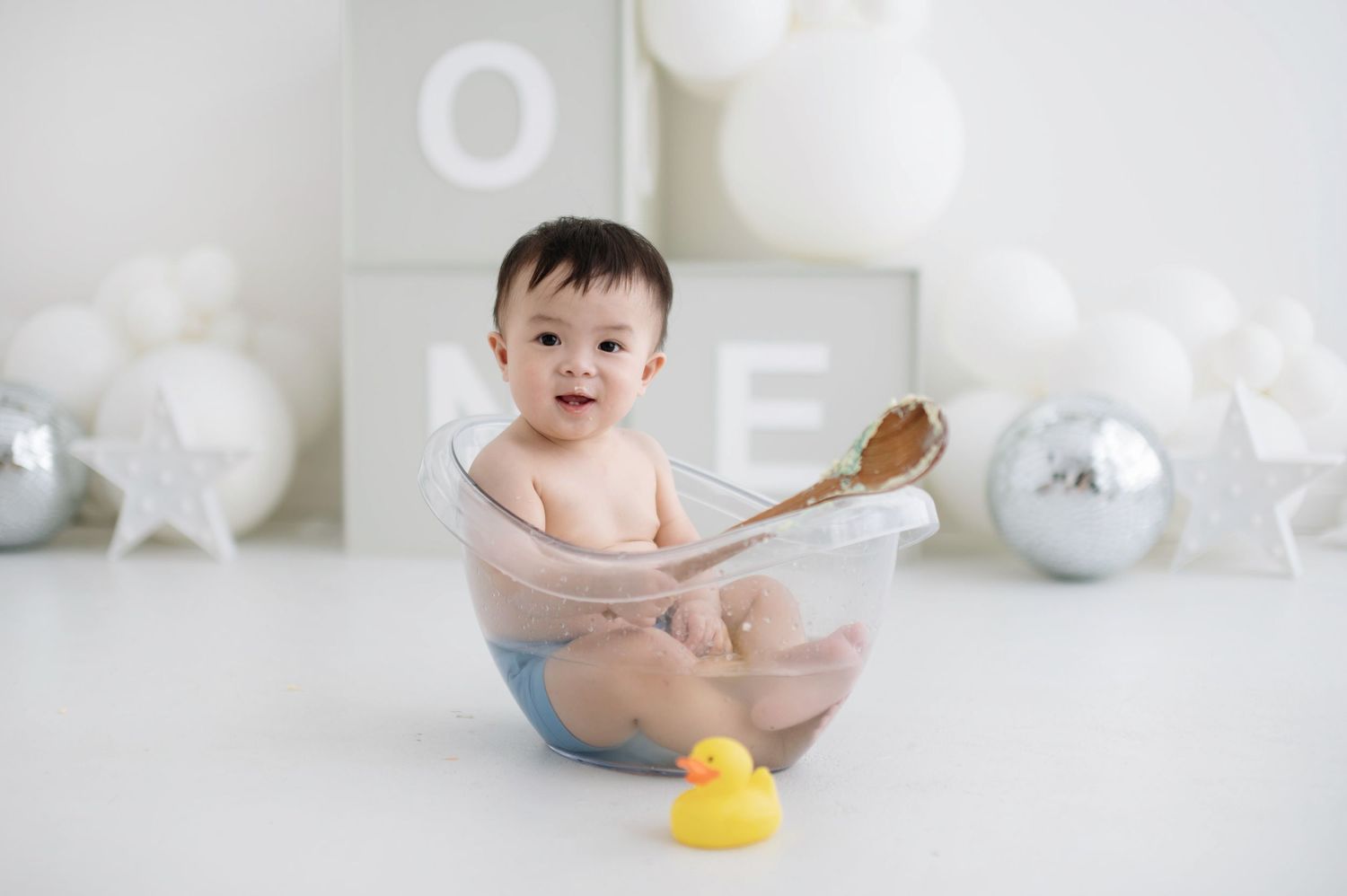 A baby sits in a white bathtub surrounded by bubbles and bath toys during bathtime.