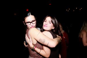 Two friends embrace and laugh together while dancing at a dark party venue.