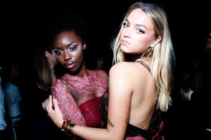 Two models pose together in elegant red and white evening wear against a dark background.