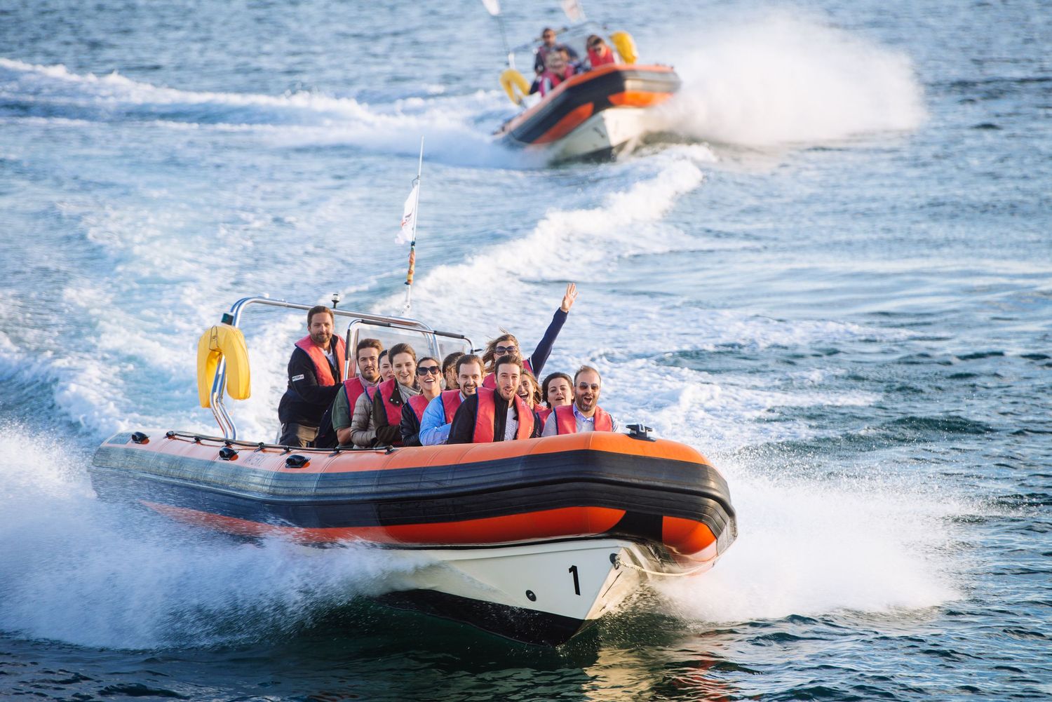 Orange speedboat carrying passengers across blue ocean waters creating white wake.