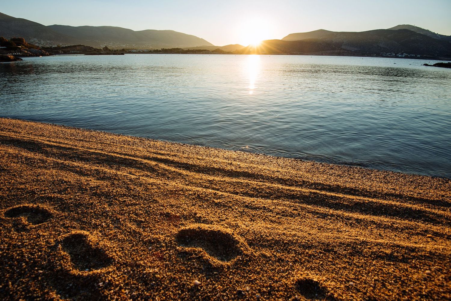 Sunset over beach with golden light reflecting on sandy shoreline.