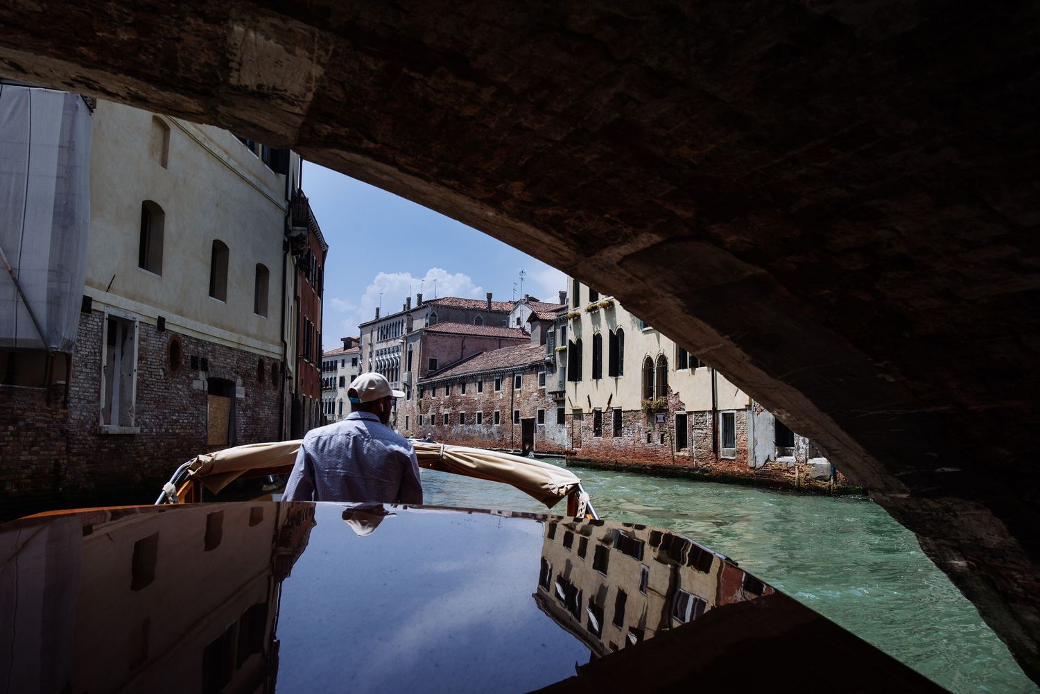 Historic buildings and narrow canals of Venice reflect in calm waters during daytime.
