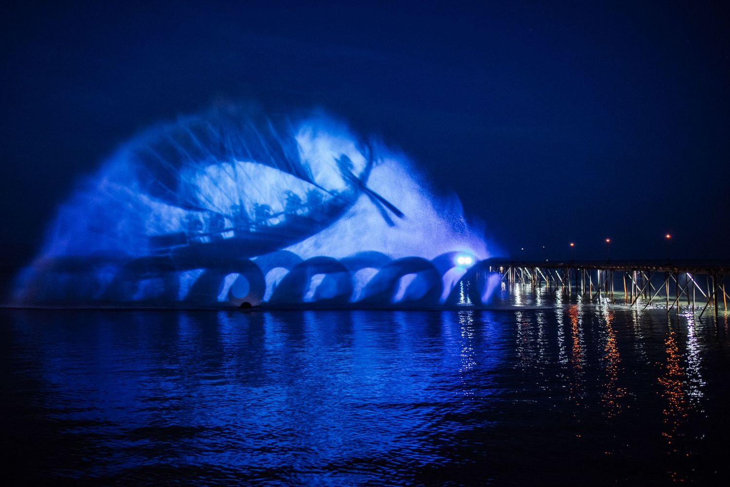 Blue illuminated glaciers and icebergs reflect on dark water at night.