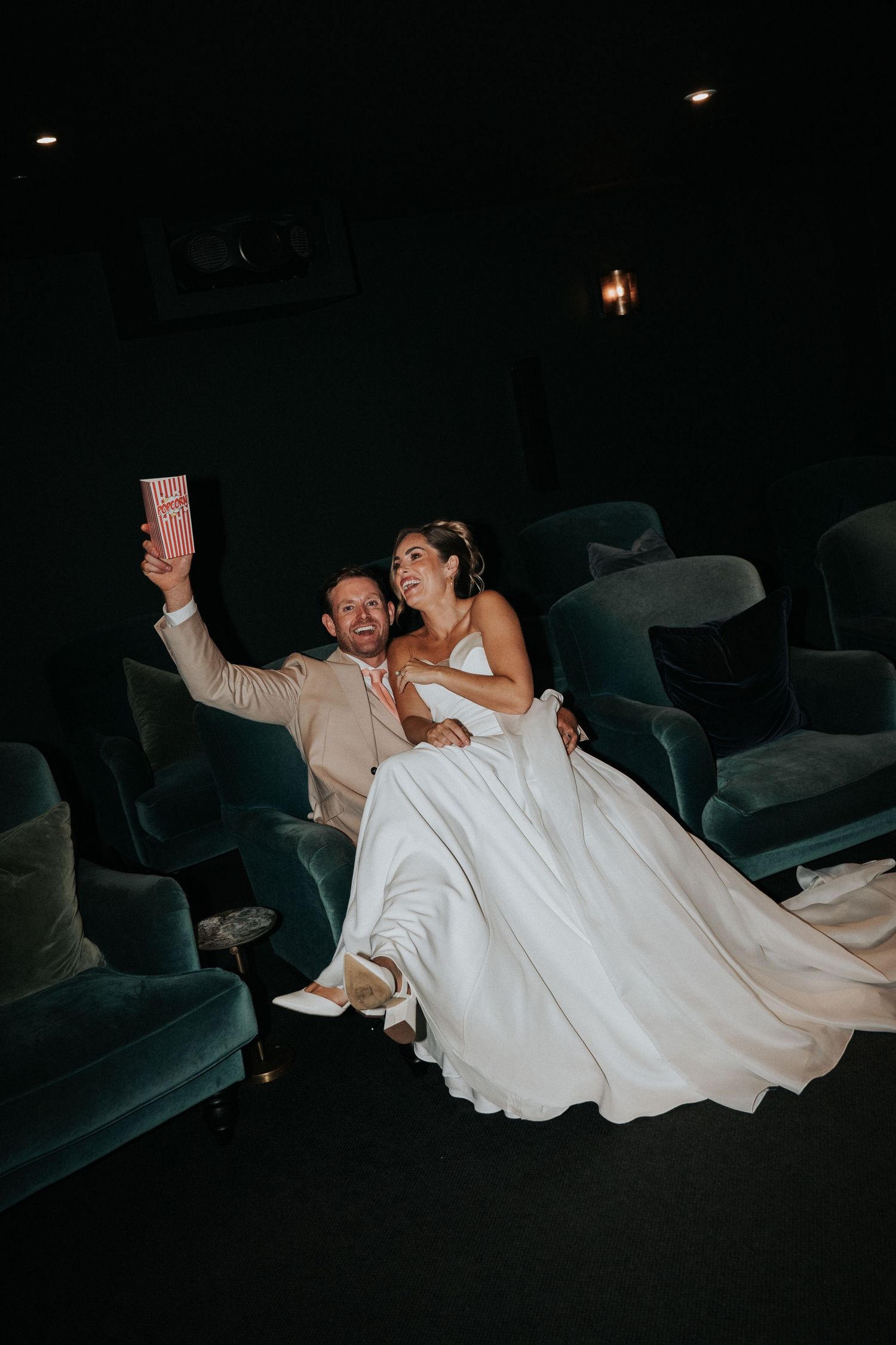 Bride and groom laughing together in the private cinema at Gara Rock Hotel during a styled wedding shoot, capturing a playful, relaxed momen