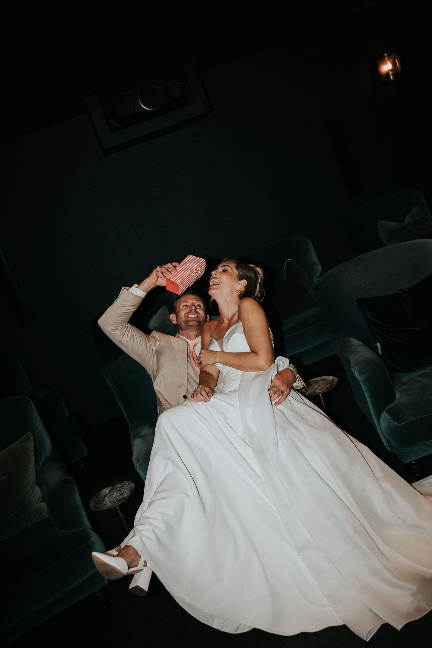 Bride and groom sharing a fun, candid moment with popcorn in the private cinema at Gara Rock Hotel, photographed during a relaxed coastal st