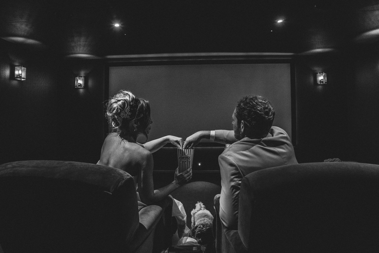 Black and white cinematic wedding portrait of a bride and groom sharing popcorn in the private cinema at Gara Rock Hotel