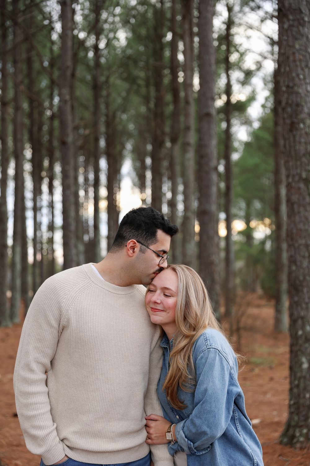 Romantic couple in casual attire sharing tender moments in a peaceful pine forest setting.