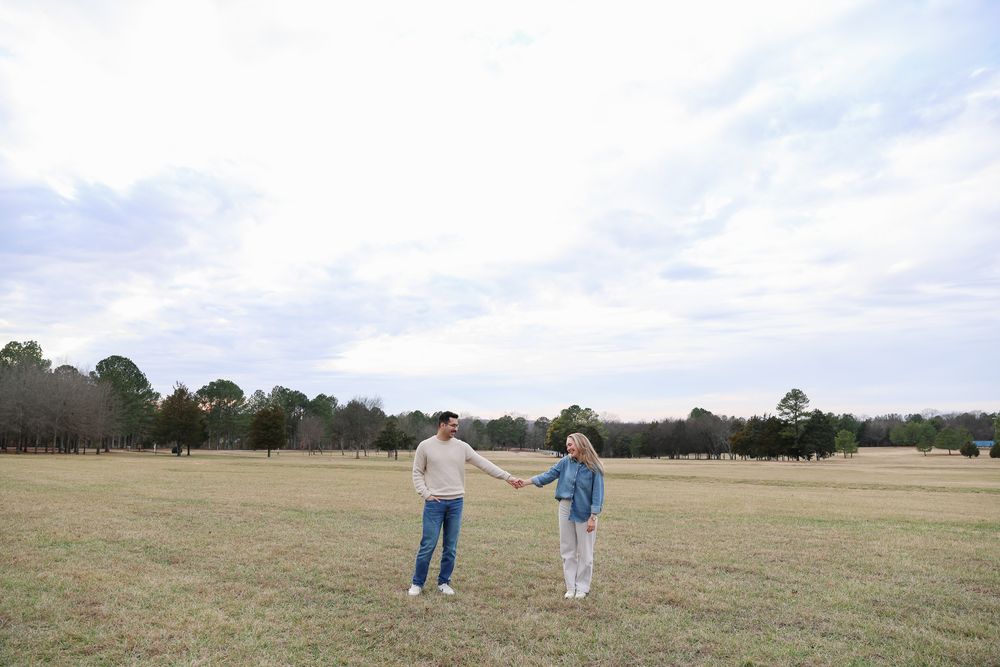 Wide landscape view of a couple walking together in a vast open field under cloudy skies.