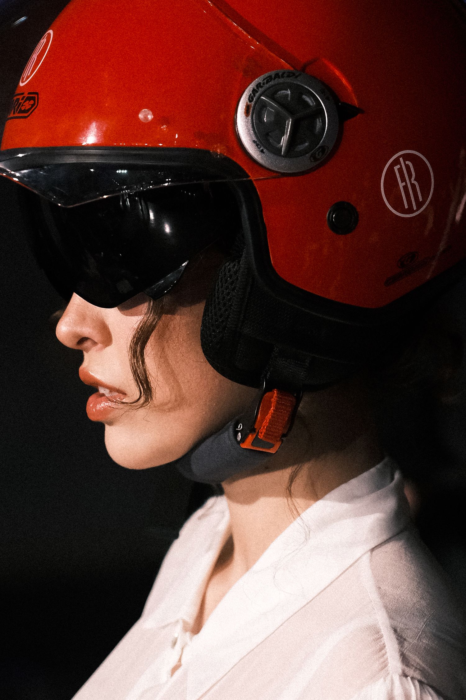Person wearing a bright red motorcycle helmet and white shirt shown in profile against dark background.
