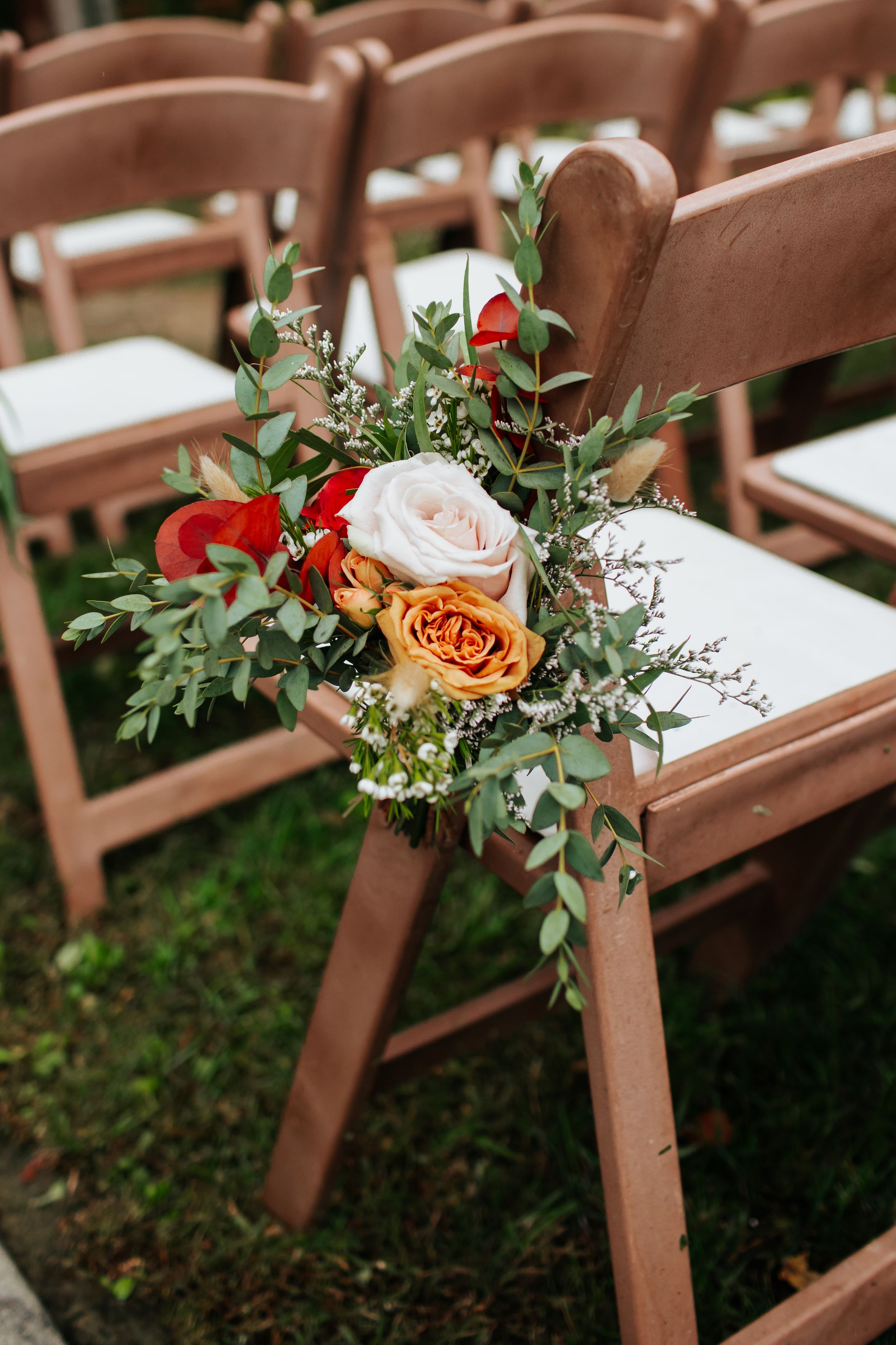 Wedding ceremony chairs decorated with romantic floral arrangements of roses and greenery along the aisle.
