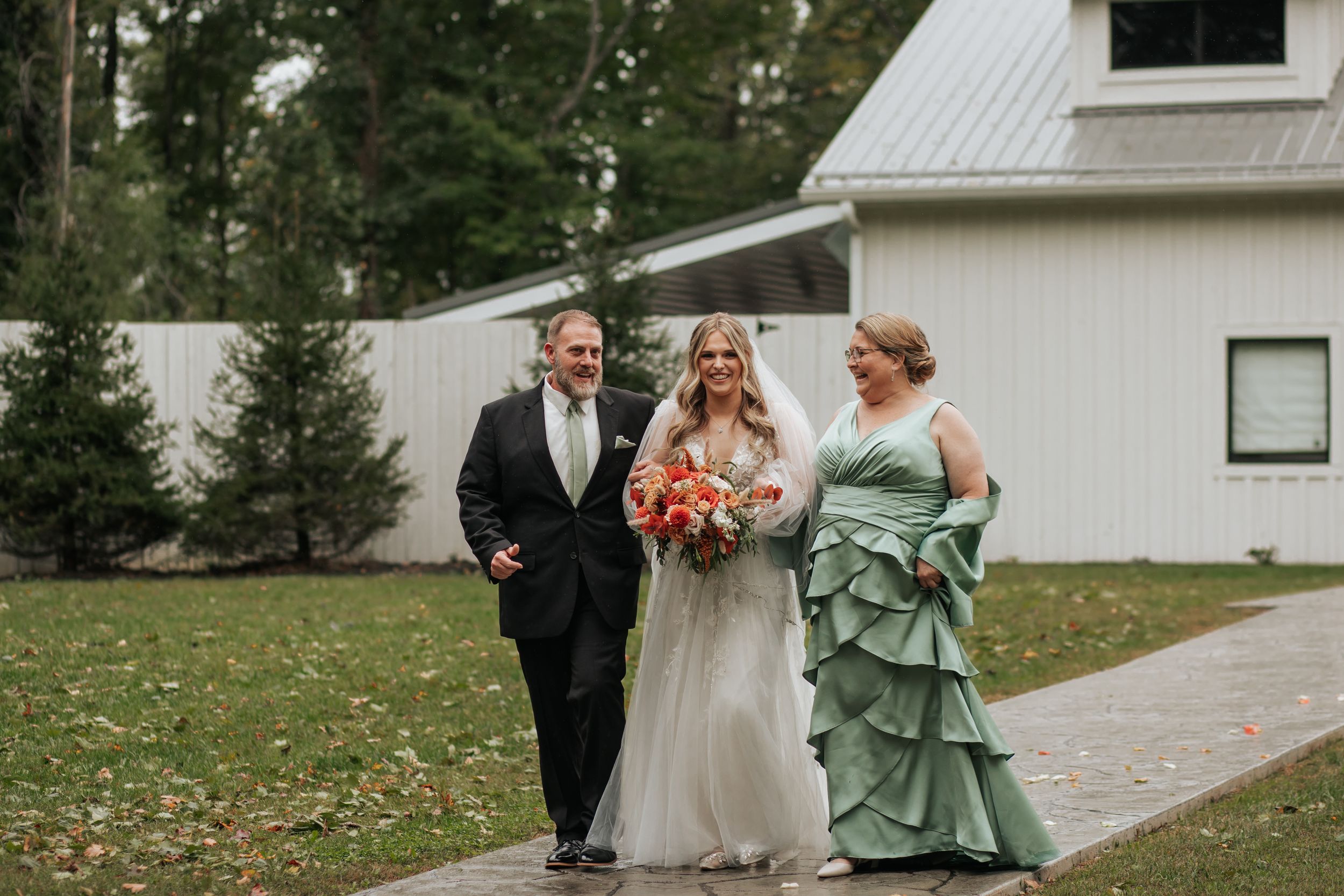 Wedding party stands outside a white building with sage green bridesmaid dresses and formal attire.