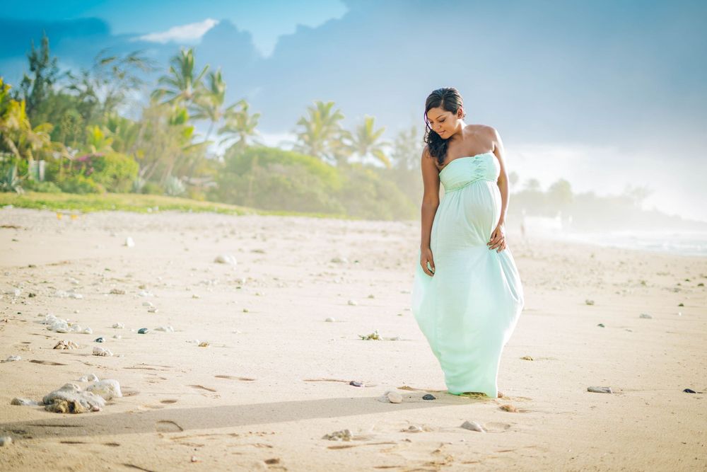 Woman in flowing mint dress walks along tropical beach at sunset.