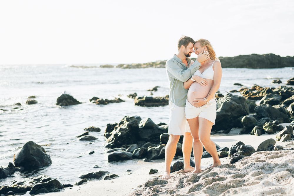 Loving couple embraces on rocky beach during sunset photoshoot.