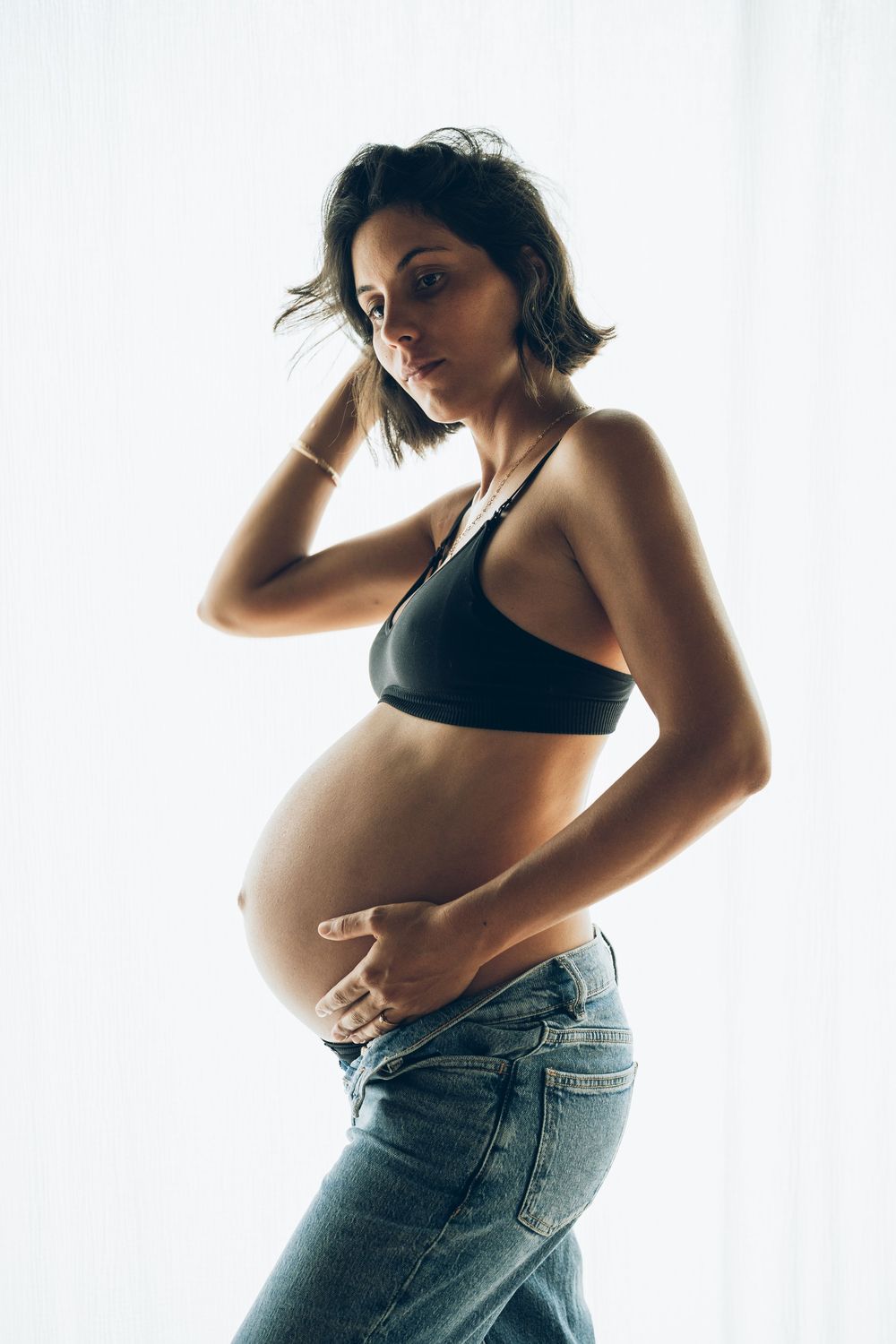 A series of artistic maternity photos showing a pregnant woman in jeans and black top against a white backdrop.