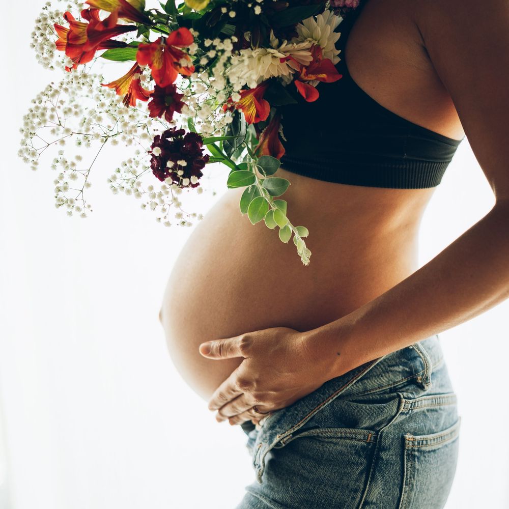 A pregnant woman's belly with a floral arrangement of red and white flowers against a white background.