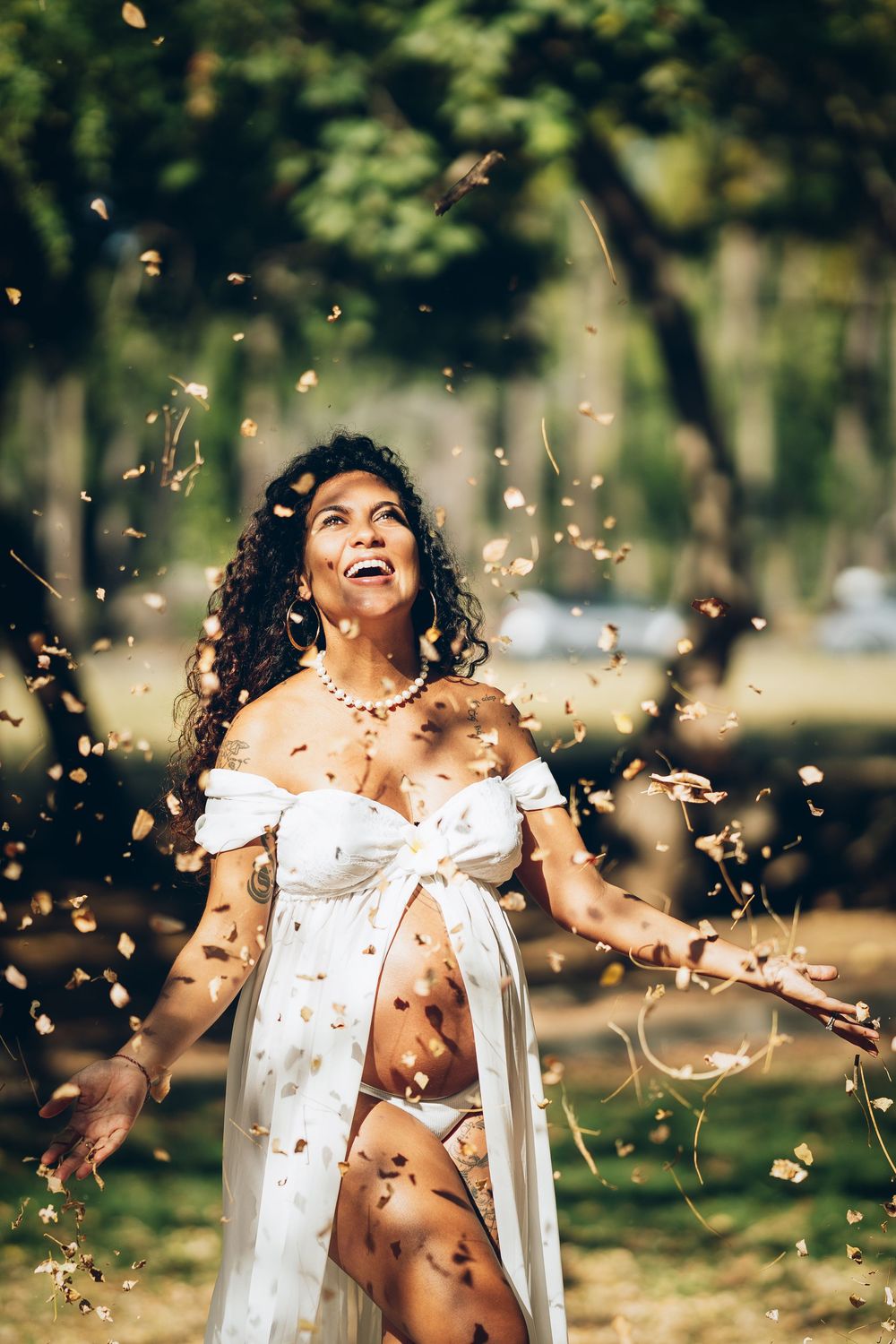 A person in a white dress twirls joyfully in a park while autumn leaves fall around them in golden sunlight.